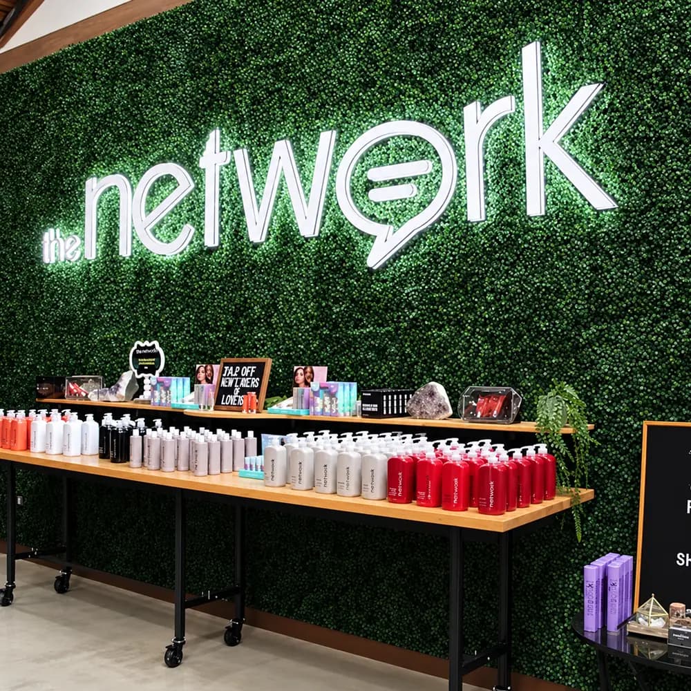The Network's illuminated sign on a green living wall above its hair care products